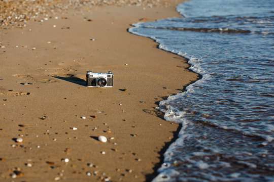 camera lies on a sandy beach near the sea. camera beach sea sand water