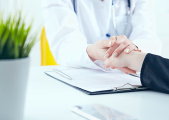 Friendly female doctor's hands holding female patient's hand for encouragement and empathy...