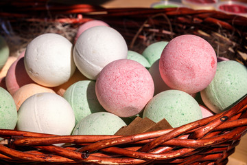 Multicolored balls of homemade soap lie in a wicker basket with straw on a sunny day. Copy space