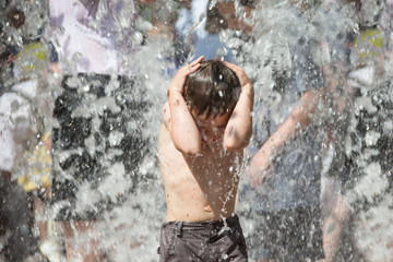Fototapeta premium Little boy under the water jets. The child bathes in the fountain. Man in the rain.Bathing in the fountain