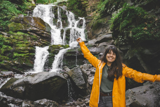 woman standing in yellow raincoat and looking at waterfall