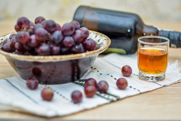 Cognac or Brandy in a glass and fresh grapes, bottle, still life in rustic style, vintage wooden background, selective focus.