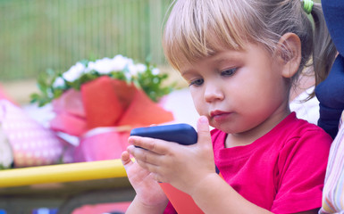 Baby girl holding a mobile phone. Little Caucasian girl playing with smartphone in summer park. Child learning how to use modern electronic devices