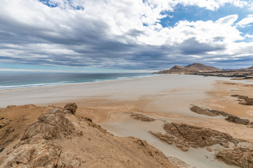 An idyllic beach at a remote location inside an arid landscape at Atacama Desert coast. The waves coming from the Pacific Ocean crash the rocks of the desert on an amazing wild dry scenery
