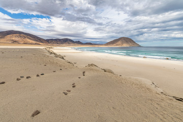 An idyllic beach at a remote location inside an arid landscape at Atacama Desert coast. The waves coming from the Pacific Ocean crash the rocks of the desert on an amazing wild dry scenery
