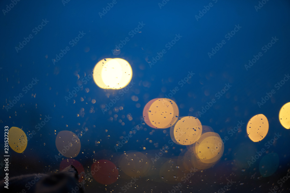Poster blurred abstract background. defocused bokeh of evening road with lanterns raindrops on the car wind