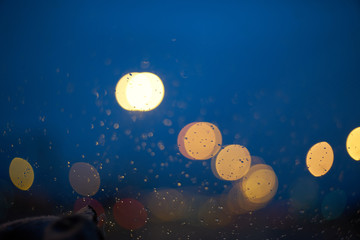 Fototapeta na wymiar Blurred abstract background. defocused bokeh of evening road with lanterns raindrops on the car window