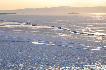 Cracks on the surface of the blue ice. Frozen lake in winter mountains. It is snowing. Lake Baikal. Winter
