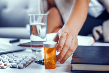 Hand with a ring on the index finger takes the orange container with pills. Other medicines are on the table in blasters. Medical concept.