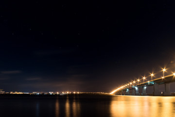 Night cityscape with luminous bridge over wide river and starry dark sky