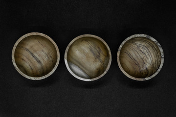 Three brown bowls made from palm tree wood placed in line on black background