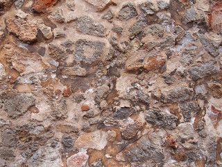 ancient weathered irregular brown rough stone wall background with textured cement in between the rocks