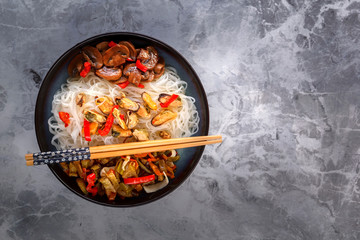 Traditional Asian food - rice noodles with seafood, salad, red pepper and fried mushrooms are on the side table. Copy space. Top view