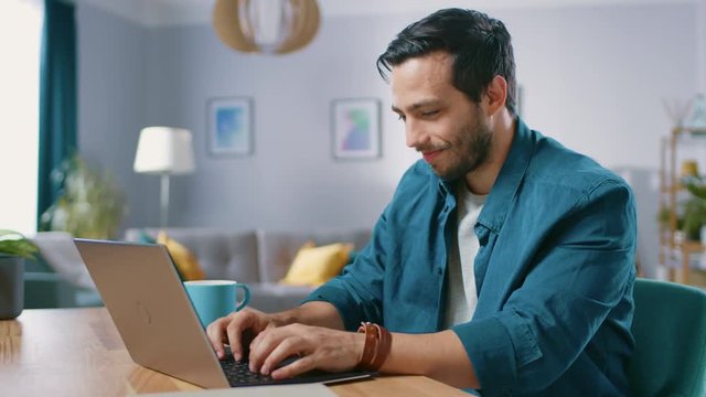 Portrait of Handsome Young Man Using Laptop Computer at Home, Watching and Laughing at Content. Happy Hispanic Man Works on Computer.