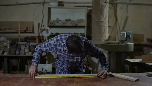 Worker in work shirt measures wooden board with long yellow ruler on a workbench