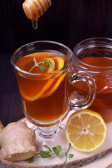 Tea with lemon and mint in a glass. Honey is dripping from the wooden spoon