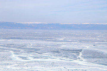 Naklejka na ściany i meble Cracks on the surface of the blue ice. Frozen lake in winter mountains. It is snowing. Lake Baikal. Winter