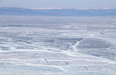 Cracks on the surface of the blue ice. Frozen lake in winter mountains. It is snowing. Lake Baikal. Winter