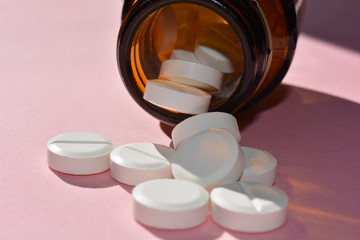 white pills and bottle on pink background
