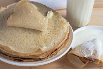 Fried pancakes with butter, a glass of milk, sour cream on a wooden table.