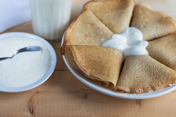Fried pancakes with butter, a glass of milk, sour cream on a wooden table.