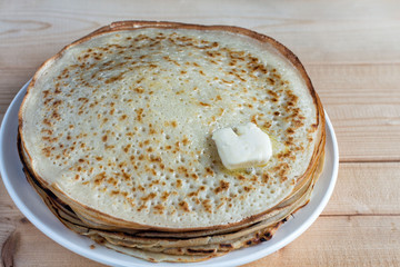 Fried pancakes are stacked on a plate on a wooden table.