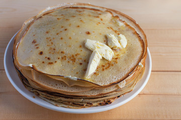 Fried pancakes are stacked on a plate on a wooden table.