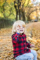 little girl with blue eyes sitting on fallen leaves and playing fun