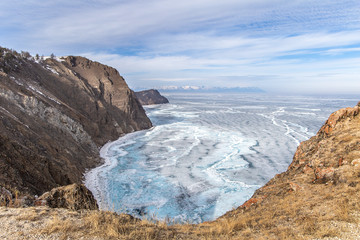 Lake Baikal in winter. Beautiful rocky island on a background of blue sky and smooth ice with cracks