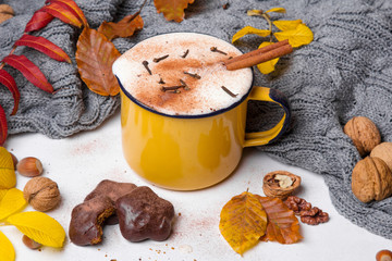 Kubek kawy z goździkami i cynamonem otoczony jesiennymi liśćmi i ciepłym szalem. 