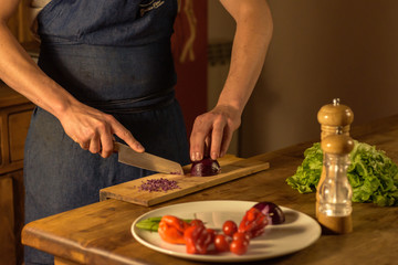 Chef cutting green onions on wooden board in dim light.