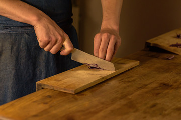 Chef cutting green onions on wooden board in dim light.