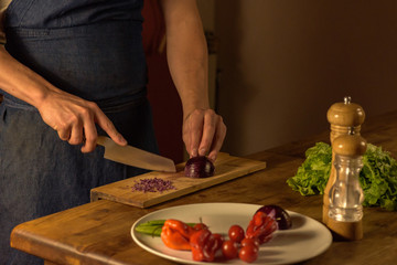Chef cutting green onions on wooden board in dim light.
