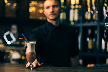 Cocktail is on the bar counter. Bartender is on background