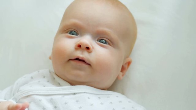 A cute little baby is looking into the camera and is happy on a white bed.