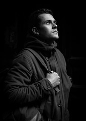 Young hipster man in casual wear standing in the dark. A thin man in a warm jacket and backpack. Conceptual black and white photography.