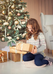Fototapeta na wymiar Happy Holidays. Cute little baby opens a Christmas present. Girl happy gifts sitting at the Christmas tree.
