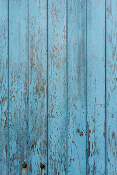 Peeling blue paint on decaying wood panel fence/door
