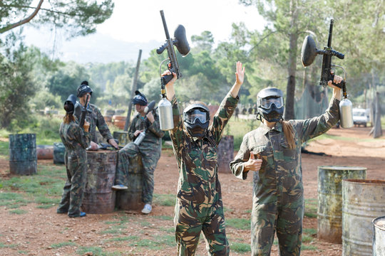 Cheerful young women in camouflage holding guns ready for playing paintball