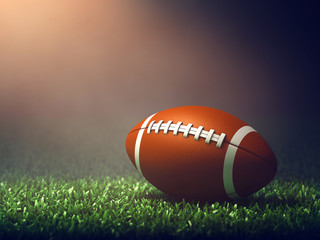 American football ball on grass field lit by spotlight, Game night