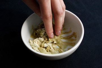 Close up of Man's hand preparing wasabi from wasabi powder and water in a white ceramic bowl. Isolated on black background.