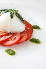 Sliced tomato, mozzarella, pesto and basil  leaves on a gourmet plating. Fresh dish isolated on white. Close-up detail of spring salad.