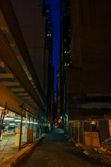 Dark and scary downtown urban city street alley next to an eerie illuminated parking garage and spooky empty lot at night