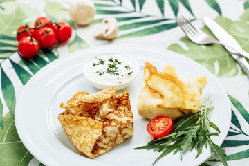 Rolled Delicious Crepes stuffed with chicken and mushrooms on the white plate serving with sour cream. Pancake is a flat cake, often thin and round, prepared from a starch based batter that may