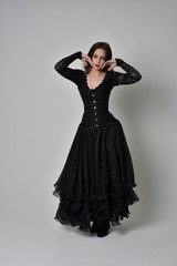 Fototapeta premium full length portrait of brunette girl wearing long black gown with corset. standing pose on grey studio background.