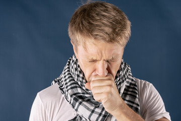 Man with cold and flu illness suffering from a headache and cough. Blue background