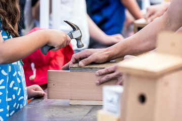 Young girl child with a hammer building bird house with a help of an adult.