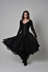 full length portrait of brunette girl wearing long black gown with corset. standing pose on grey...