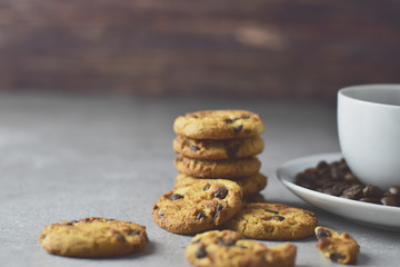 Black coffee in a white cup with plate and coffee beans and chocolate chips cookies beside on top of a rustic concrete table top in vintage tone, quick breakfast and morning freshness