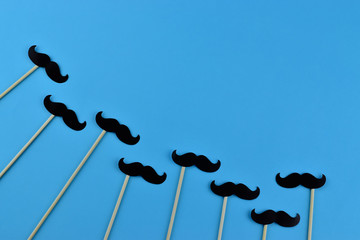 Black mustaches on light blue background representing an annual event involving the growing of...